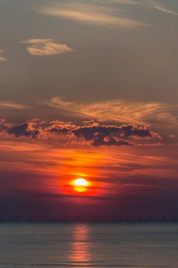 turuncu kırmızı günbatımı güzel gökyüzü, bulutlar ve ufukta yel değirmenleri denizleri yansıtıyor.