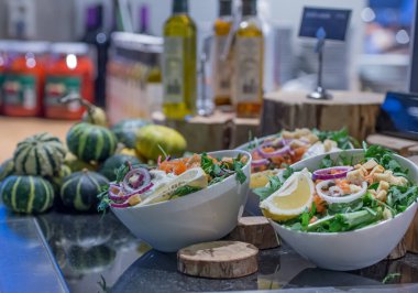 Arkaplanda soğanlı ve limonlu roka ve balkabağı ile zeytinyağı ve diğer soslu salata barı.