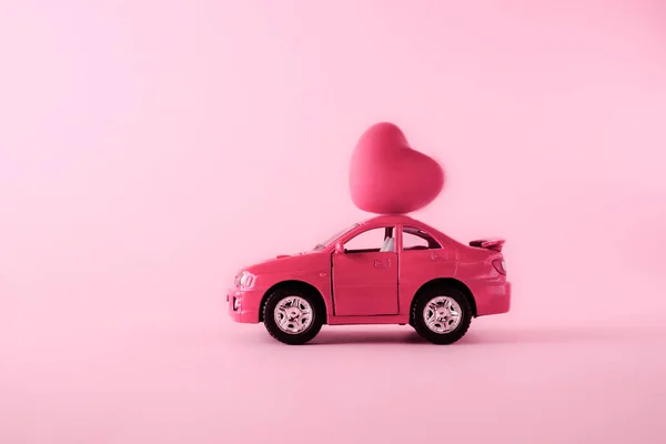 Pink toy car with hearts on a pink background. Postcard February 14, Valentine\'s Day. Flower delivery. March 8, International Women\'s Day, birthday