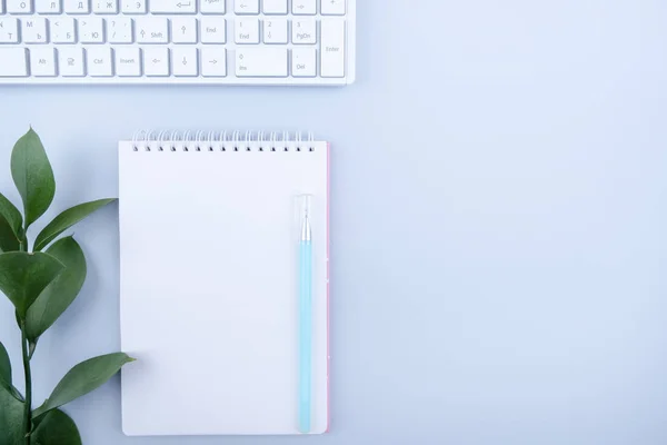 Düz yatıyordu, üst görünüm ofis masası yazma masası. Boş not defteri, klavye, mavi arka plan üzerinde yeşil sayfa ile çalışma alanı.