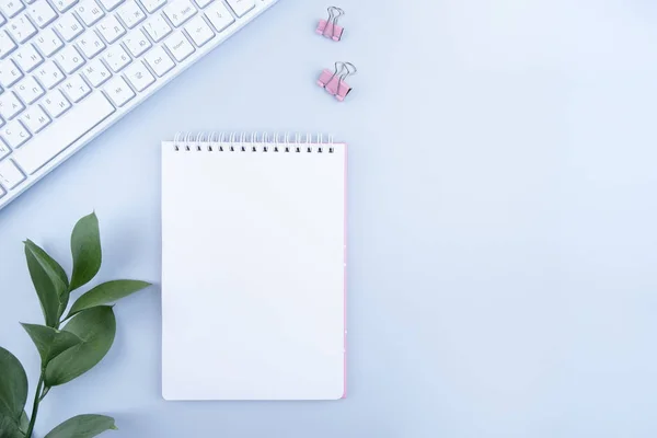 Dümdüz uzanmış, üst kattaki ofis masasında yazı masası. Çalışma alanı boş defter ve kırtasiye malzemesi, klavye, mavi arkaplanda yeşil sayfa.