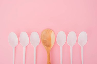 Plastik kaşıkların arasında tahta bir kaşık. Pembe arka plan. Farklı düşünün, bireysel olarak ve kalabalığın konseptinden uzaklaşın..