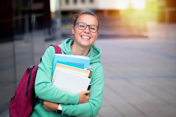 Szczęśliwa uczennica trzymająca książki w rękach. Aktywna kobieta w okularach patrzy w kamerę. Szeroki uśmiech na zewnątrz. Przestrzeń kopiowania — Zdjęcie stockowe