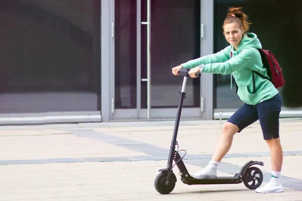 Bella ragazza o donna in sella elettro scooter con zaino e guardare direttamente alla fotocamera, moderno trasporto ecologico — Foto Stock