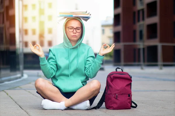 Lotus pozisyonunda oturan ve kafasında bir yığın kitapla meditasyon yapan bir kız öğrenci..