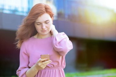 Kızıl saçlı güzel kadın akıllı telefonuna bakıyor. Pembe elbiseli ciddi kız dışarıda bir mesaj okuyor.