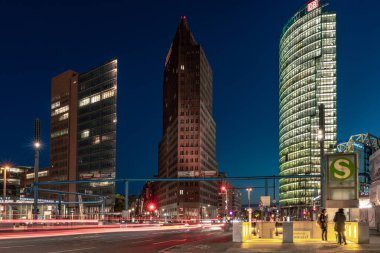 Berlin, Almanya - 12 Mayıs 2019: Potsdamer Platz'ın gün batımında araba ışıkları ve toplu taşıma araçlarını kullanan insanlar ile binaları.
