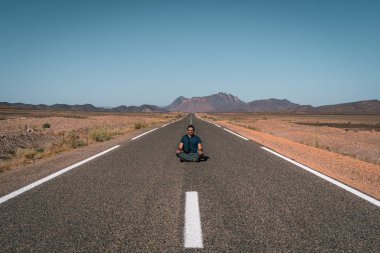 Adam fotoğraf için poz veriyor, çölde boş asfalt yolda.