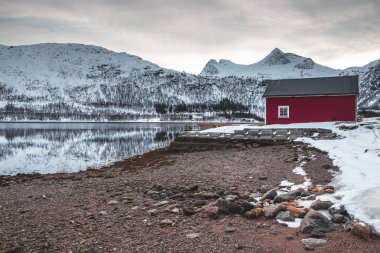 Dağların üstündeki göldeki kırmızı ev. Norveç, Lofoten Adaları 'nın muhteşem manzarası