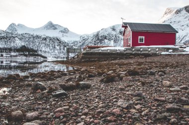 Dağların üstündeki göldeki kırmızı ev. Norveç, Lofoten Adaları 'nın muhteşem manzarası