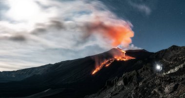 Volkan Etna 'nın panoramik görüntüsü dolunay ile birlikte gecenin çarpıcı bir patlaması sırasında. Manzarayı meşaleyle aydınlatan bir adam, Sicilya, İtalya, Catania.
