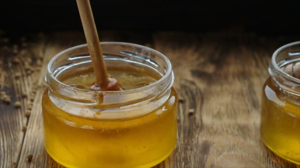 Мед в стеклянной банке с деревянным медовым ковшом на деревянном столе — стоковое видео