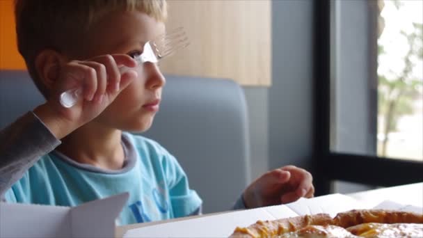 En liten pojke på fyra år skär en pizza med en plast kniv — Stockvideo