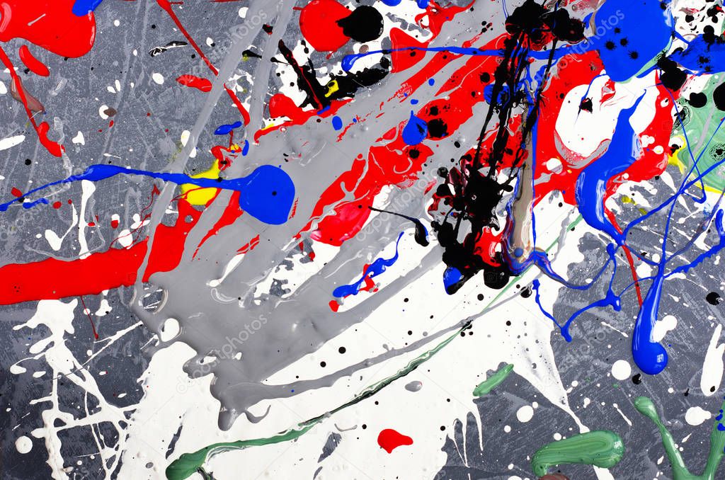 a spot of white and black and yellow and green and red and blue spilled paint on a concrete textured surface.