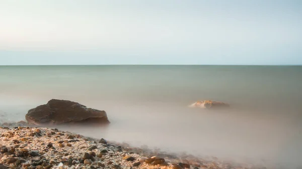 Lunga esposizione paesaggio marino. in primo piano pietre — Foto Stock