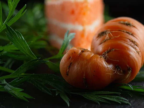 Hässliche frische Karotten mit grünen Blättern. Im Hintergrund ein Karottenkuchen. — Stockfoto