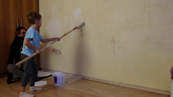 Ένα πεντάχρονο αγόρι ζωγραφίζει έναν τοίχο με σχέδια λευκής μπογιάς. Δίπλα του είναι ο πατέρας του.. — Αρχείο Βίντεο
