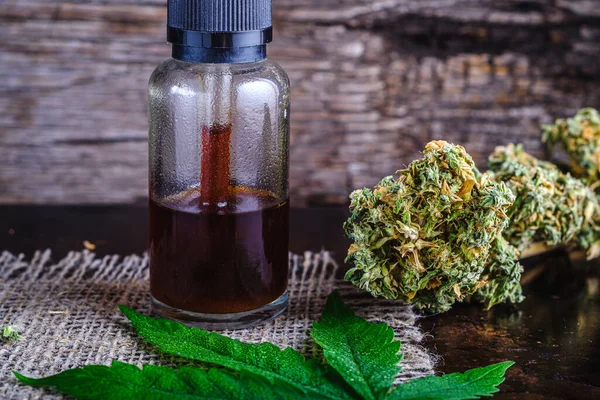 Kahverengi tıbbi kenevir reçinesi özü ilaç atıcısının içinde. Ürün, kenevir özütü tetrahydrocannabinol ve kenevir içeriyor. Marihuana tomurcukları ve kenevir yaprağının yanında. Kenevir çuvalında. Paslı metal yüzeyinde ahşap zemin. yatay