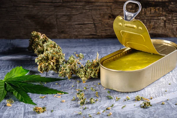 Marihuana tomurcukları. Tıbbi kenevir yağı açık bir teneke kutuda. Kenevir yaprakları. yatay oryantasyon. Beton alçı ahşap arka planda. yatay orinasyon.