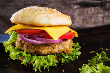 Taze lezzetli ev yapımı vejetaryen burger, sade ahşap arka planda, doğal bir levhada yatar. Marul, peynir, soğan ve domatesli lezzetli hamburger. Karabuğday ve mercimek pirzolası. yatay orinasyon