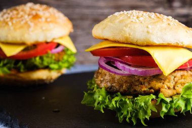 İki taze nefis ev yapımı sebzeli burger, sade ahşap arka planda doğal bir tahta üzerine uzanır. Marul, peynir, soğan ve domatesli lezzetli hamburger. Karabuğday ve mercimek pirzolası. yatay orinasyon