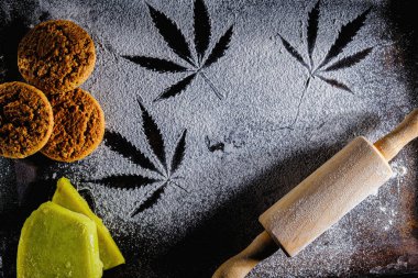 Un üzerinde marihuana yaprağı, merdane, üç kurabiye ve kenevir yağı. Paslı bir tavada. En üstteki düz yerde. Yatay yönelim