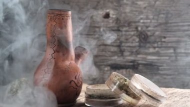 Üzerinde öğütücü ve büyük bir tıbbi esrar tomurcuğu olan esrar dolu dumanı tüten bir nargile. Ahşap arka plan. 4k