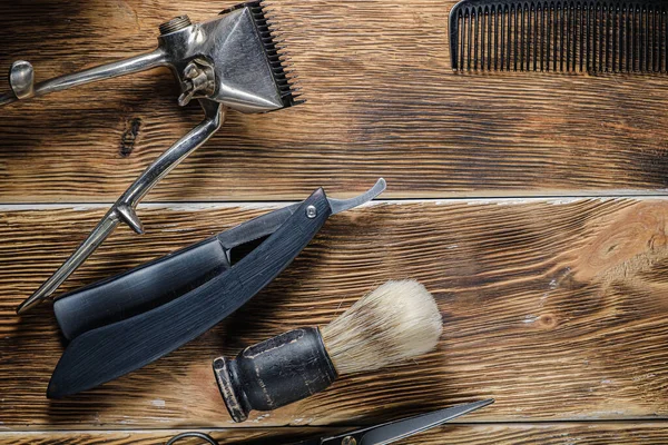 old hand hairdressing tools. Manual clipper, hairdressing scissors, straight razor, brush for shaving foam. on brown weathered wood background. top view flat lay. Horizontal orientation.