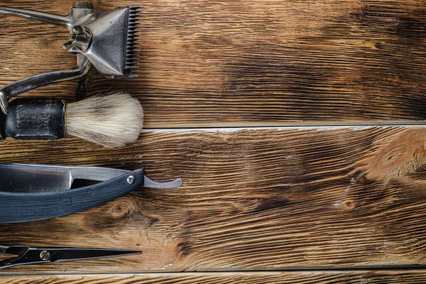 old hand hairdressing tools. Manual clipper, hairdressing scissors, straight razor, brush for shaving foam. on brown weathered wood background. top view flat lay. Horizontal orientation. copy space.