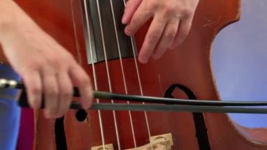 Erkekler yayla bas çalıyor. Kapat. Erkek müzisyen yay tekniği uyguluyor. Klasik konserde kontrabass ritim. Akustik bas enstrümanı