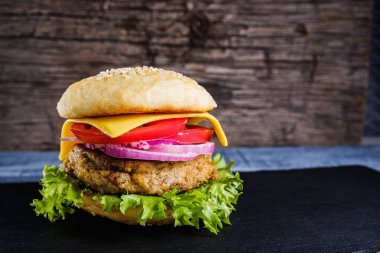 Taze lezzetli ev yapımı vejetaryen burger, sade ahşap arka planda, doğal bir levhada yatar. Marul, peynir, soğan ve domatesli lezzetli hamburger. Karabuğday ve mercimek pirzolası. yatay orinasyon