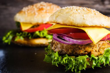 İki taze nefis ev yapımı sebzeli burger, sade ahşap arka planda doğal bir tahta üzerine uzanır. Marul, peynir, soğan ve domatesli lezzetli hamburger. Karabuğday ve mercimek pirzolası. yatay orinasyon