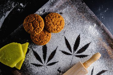 Un üzerinde marihuana yaprağı, merdane, üç kurabiye ve kenevir yağı. Paslı bir tavada. En üstteki düz yerde. Yatay yönelim