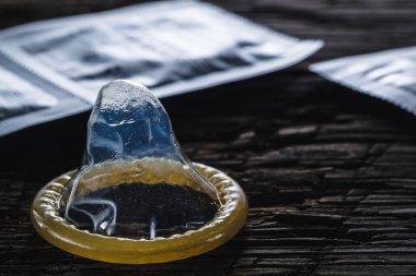 Dünya cinsel cehennem günü. Paketlenmemiş prezervatif eski ahşap bir arka planda paketlenmiş konilerin yanında duruyor. dramatik kare. kopyalama alanı. yatay yönelim.