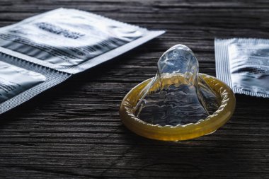 Dünya cinsel cehennem günü. Paketlenmemiş prezervatif eski ahşap bir arka planda paketlenmiş konilerin yanında duruyor. dramatik kare. kopyalama alanı. yatay yönelim.