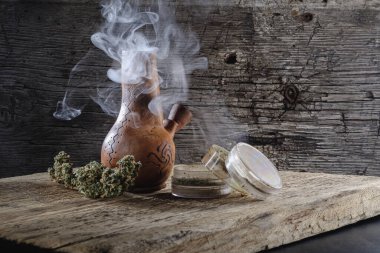 Ahşap bir yüzeyde tıbbi esrar tüttürmek. Yakında bir öğütücü ve marihuana tomurcuğu var. Karanlık çerçeve. Yatay yönelim.