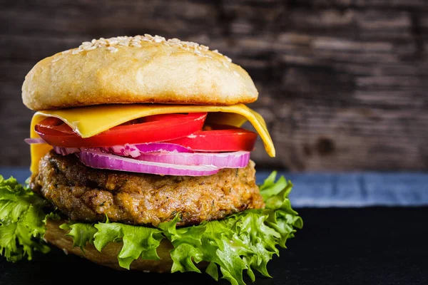 Taze lezzetli ev yapımı vejetaryen burger, sade ahşap arka planda, doğal bir levhada yatar. Marul, peynir, soğan ve domatesli lezzetli hamburger. Karabuğday ve mercimek pirzolası. yatay orinasyon