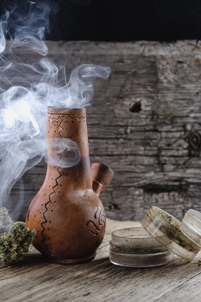 Ahşap bir yüzeyde tıbbi esrar tüttürmek. Yakında bir öğütücü ve marihuana tomurcuğu var. Karanlık çerçeve. düşey yönelim