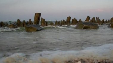 Dalgalar denizin yakınındaki harabe bir iskeleye çarpar. Gündoğumu Günbatımı. Hiç kimse. Genel plan.