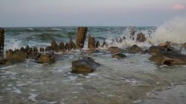 Dalgalar denizin yakınındaki harabe bir iskeleye çarpar. Gündoğumu Günbatımı. Hiç kimse. Genel plan.