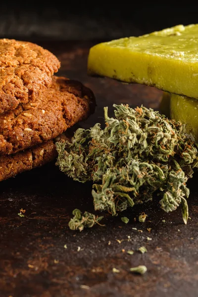 Esrarlı bisküviler, marihuana, marihuana, tereyağı ve yakın plan pas metali tomurcukları. Esrarlı sağlıklı tıbbi yiyecekler. Tomurcuklar yanlış dağılmış. Kırsal kesim. Dikey yönelim.