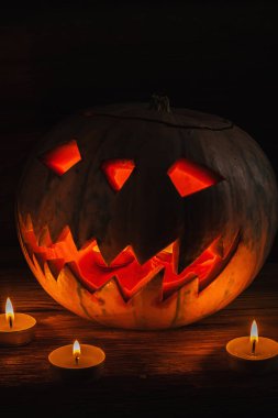 Fantezi Gecesi 'nde parlayan Jack O' Lantern. Cadılar Bayramı. Yakınlarda mumlar yanıyor. Eski ahşap arka planda. dramatik kare. düşey yönelim.