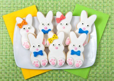 Yeşil yer paspas arka plan ile bir tabak üzerinde Paskalya Bunny Şeker Çerezler. Marshmallow fondan şeker ayak, göz ve burun ve kuyruk ve yay ile çerez kaplı. Erkek ve kız. Yeşil ve sarı peçeteler.