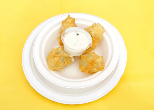 White paper plate with battered and fried artichoke with dipping sauce on a yellow table cloth. Popular street fair food.
