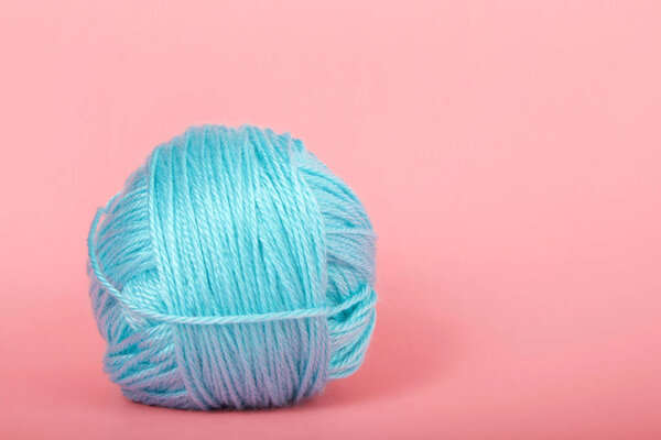 Single ball of light blue baby soft thin yarn on a light pink background.