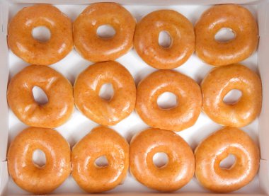 Beyaz bir kutu izole düz sırlı çörekler üst görünüm düz yatıyordu. Bir düzine çörek. Orijinal sırlı donut tarih boyunca insanların favori kalmıştır.