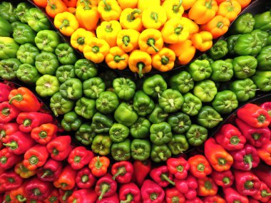 Yeşil, sarı ve kırmızı çan ve portakal biberleri göz çizimi şeklinde markete istiflenmiş..