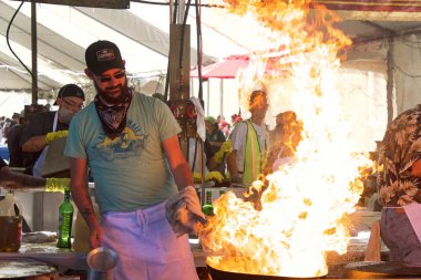 Gilroy, CA - July 27, 2019: World famous pyro chefs putting on spectacular flame up shows while preparing garlic laced calamari and scampi in huge iron skillets at the 41st annual Garlic Festival. clipart