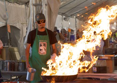 Gilroy, CA - July 27, 2019: World famous pyro chefs putting on spectacular flame up shows while preparing garlic laced calamari and scampi in huge iron skillets at the 41st annual Garlic Festival. clipart