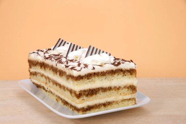 Tiramisu dikdörtgen bir tabakta, ahşap masa üzerinde, turuncu arka planda. Tiramisu, kahve, brendi ve likörle kaplı katmanlı bir İtalyan tatlısıdır..